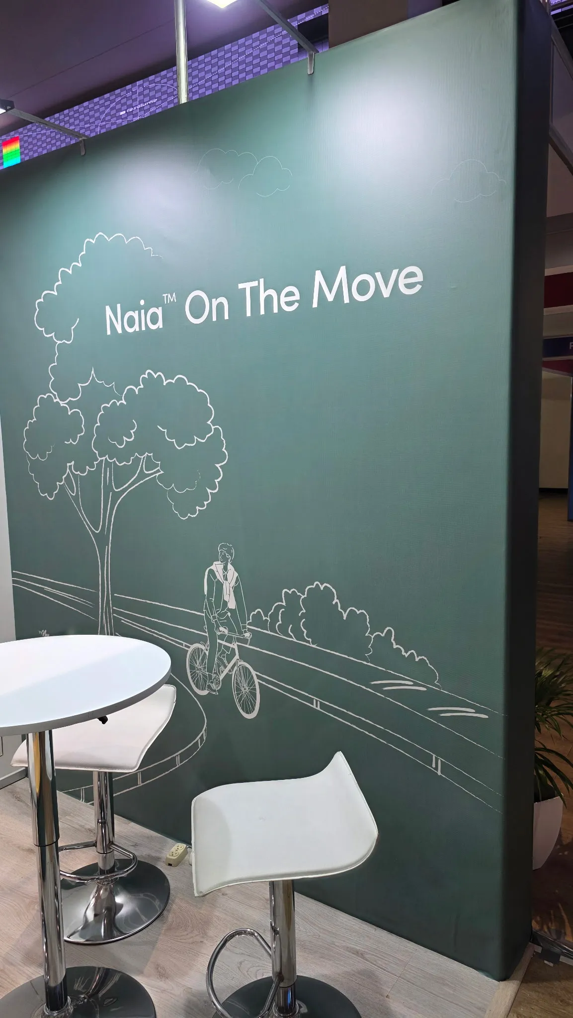 Installed green wall with a line drawing of a cyclist beneath the Naia On The Move headline.