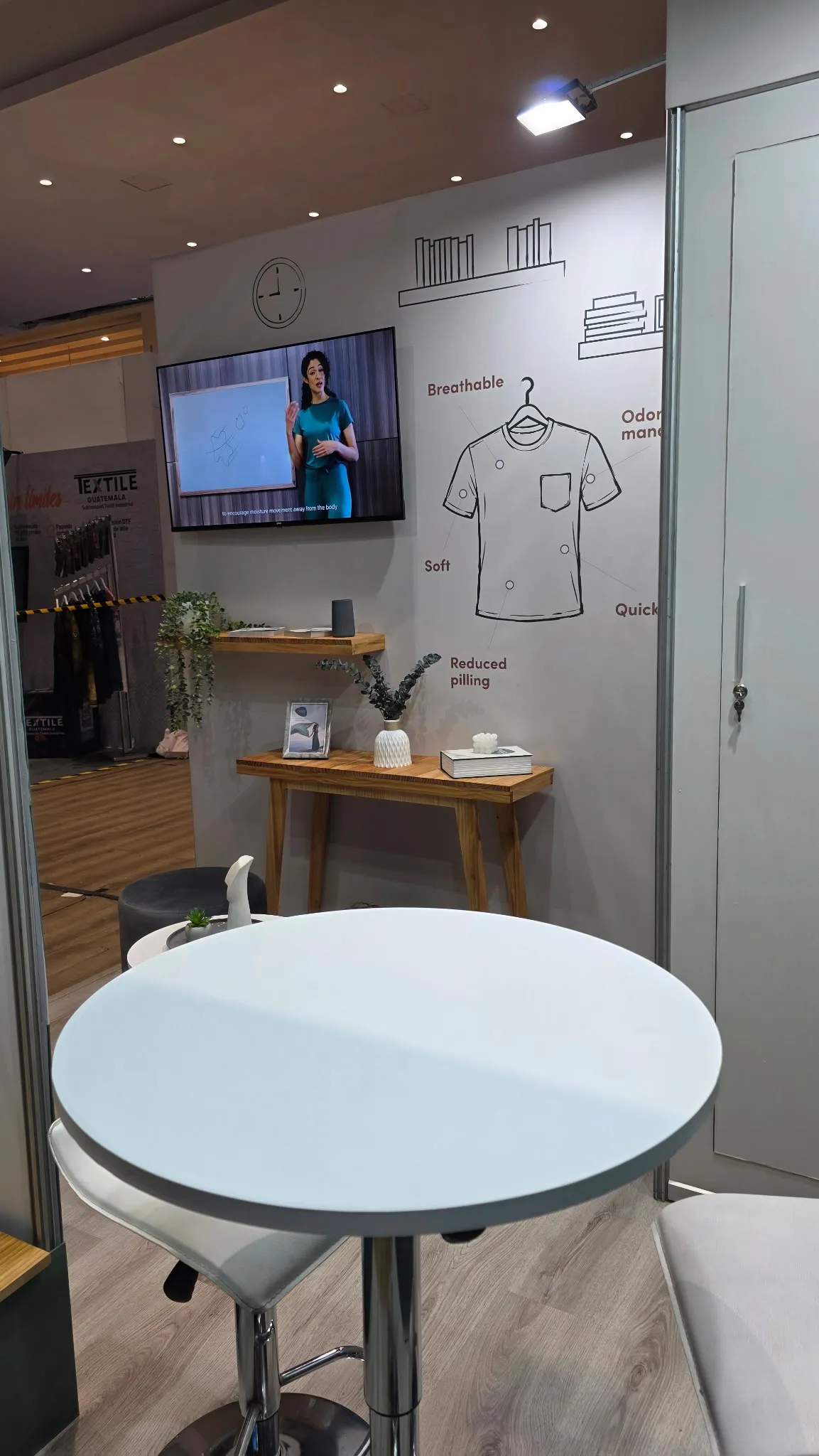 Installed cream wall with an illustrated T-shirt, product callouts, shelves, and a mounted screen.